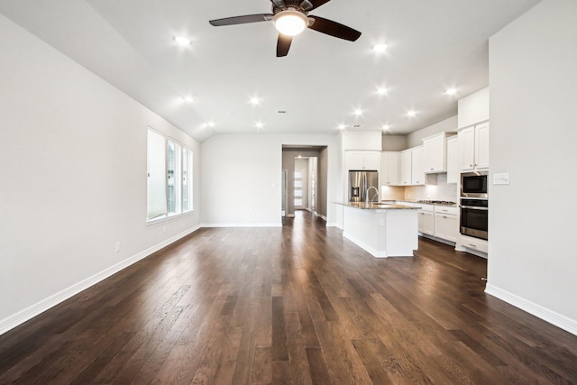 kitchen with a kitchen bar, a kitchen island with sink, stainless steel appliances, white cabinets, and dark hardwood / wood-style flooring