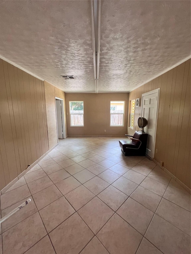 empty room with light tile patterned floors, wood walls, and a textured ceiling