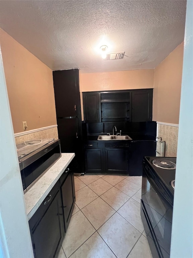 kitchen featuring light tile patterned floors, sink, tile walls, a textured ceiling, and black / electric stove