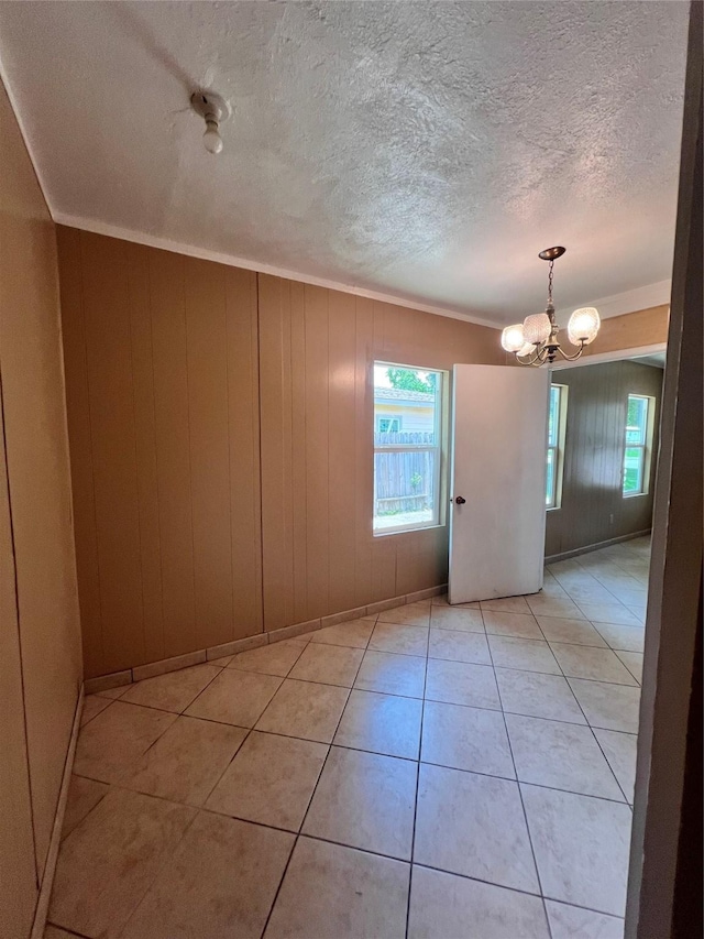 tiled empty room with plenty of natural light, crown molding, wood walls, and a notable chandelier