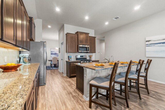 kitchen with a breakfast bar, tasteful backsplash, light wood-type flooring, stainless steel appliances, and light stone countertops