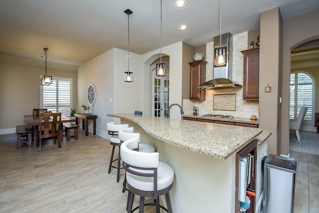 kitchen with pendant lighting, wall chimney range hood, a breakfast bar, light stone counters, and decorative backsplash