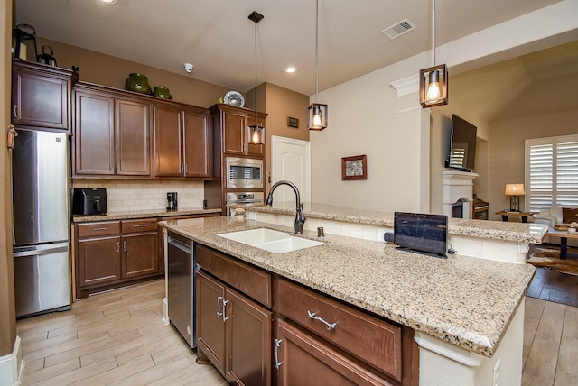 kitchen with pendant lighting, appliances with stainless steel finishes, sink, and a kitchen island with sink