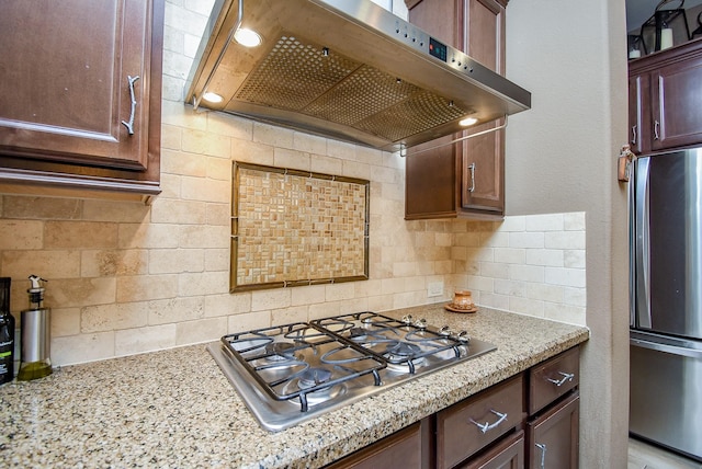 kitchen featuring tasteful backsplash, appliances with stainless steel finishes, light stone counters, and range hood