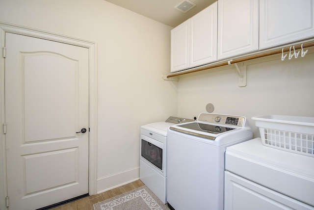 washroom featuring cabinets, washing machine and clothes dryer, and light hardwood / wood-style floors