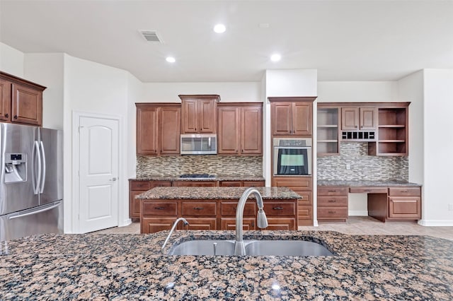 kitchen with sink, appliances with stainless steel finishes, dark stone counters, a kitchen island with sink, and decorative backsplash