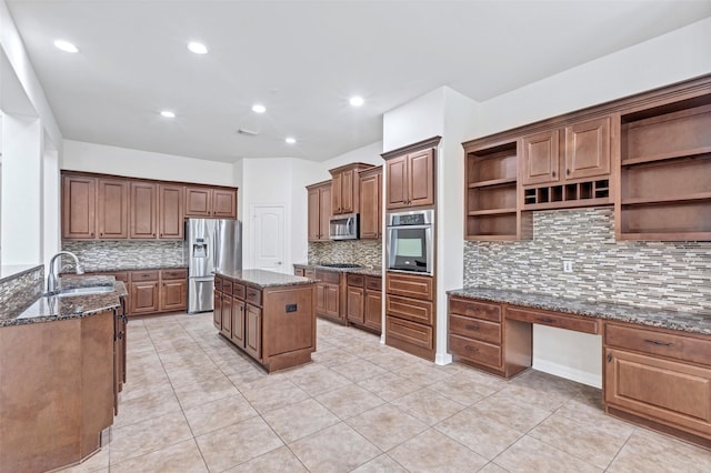 kitchen with a kitchen island, appliances with stainless steel finishes, built in desk, dark stone counters, and decorative backsplash