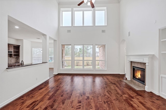 unfurnished living room featuring a towering ceiling, a fireplace, dark hardwood / wood-style floors, and ceiling fan