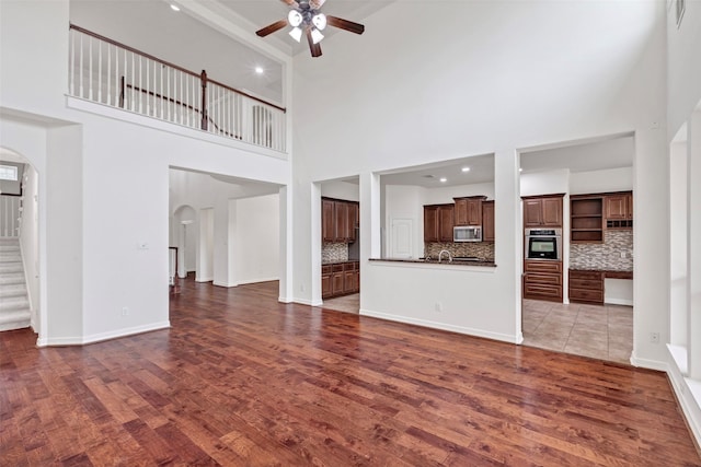 unfurnished living room featuring hardwood / wood-style flooring, a towering ceiling, and ceiling fan