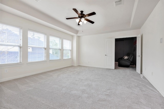 unfurnished room featuring a raised ceiling, light carpet, a wealth of natural light, and ceiling fan