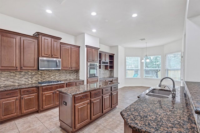 kitchen featuring sink, appliances with stainless steel finishes, a kitchen island with sink, hanging light fixtures, and tasteful backsplash