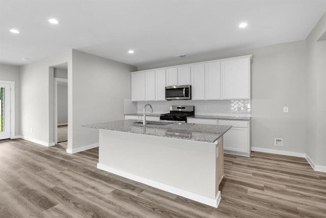 kitchen featuring a kitchen island with sink, appliances with stainless steel finishes, light stone counters, and white cabinetry