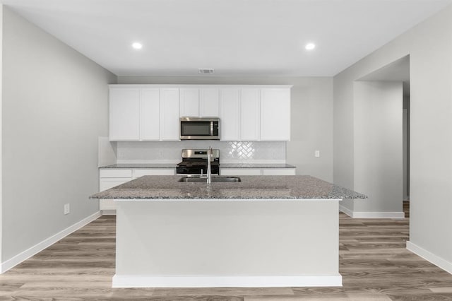 kitchen with a center island with sink, sink, appliances with stainless steel finishes, white cabinets, and light stone counters