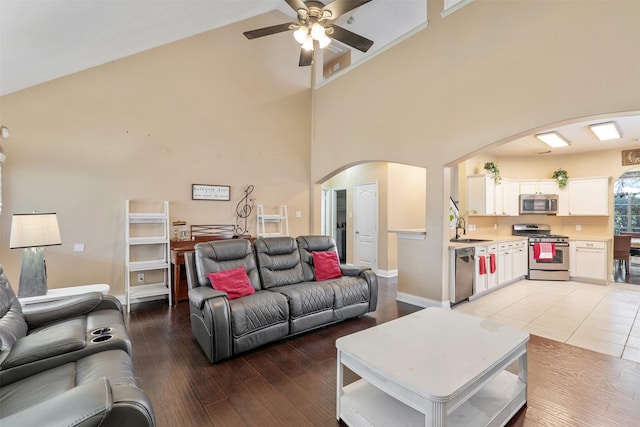 living room featuring ceiling fan, sink, a towering ceiling, and light wood-type flooring