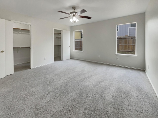 unfurnished bedroom with carpet floors, two closets, and ceiling fan