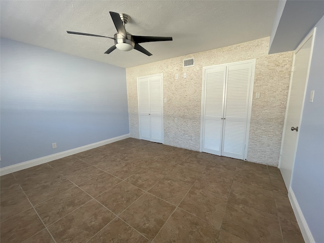 unfurnished bedroom with ceiling fan, two closets, and dark tile patterned flooring