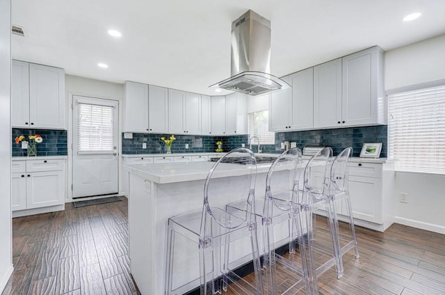 kitchen with a kitchen breakfast bar, white cabinets, and island exhaust hood