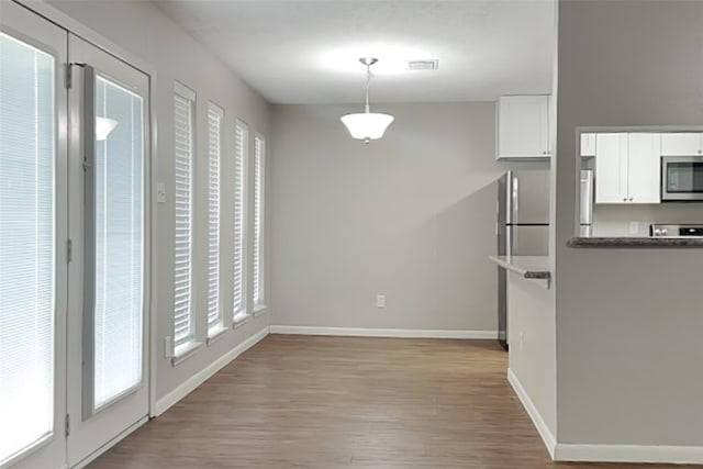 kitchen with appliances with stainless steel finishes, decorative light fixtures, white cabinetry, a healthy amount of sunlight, and light wood-type flooring