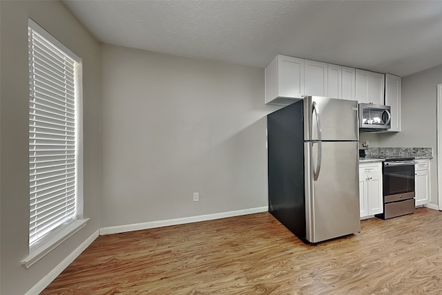 kitchen featuring light wood-type flooring, a textured ceiling, stainless steel appliances, and white cabinetry