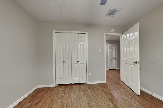 unfurnished bedroom with light wood-type flooring, ceiling fan, a closet, and a textured ceiling