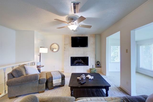 carpeted living room with ceiling fan, a tiled fireplace, and a textured ceiling