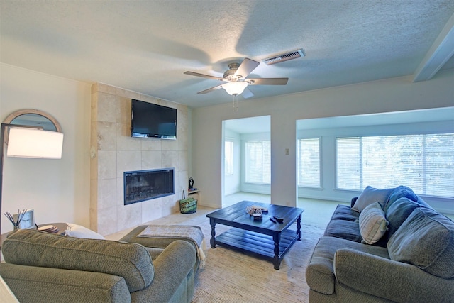 living room featuring ceiling fan, light colored carpet, a fireplace, and a textured ceiling