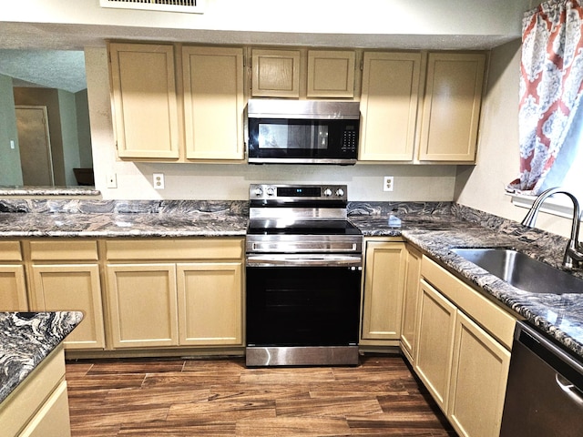 kitchen with stainless steel appliances, sink, dark stone countertops, and dark hardwood / wood-style flooring