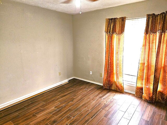 empty room with dark wood-type flooring, a wealth of natural light, a textured ceiling, and ceiling fan