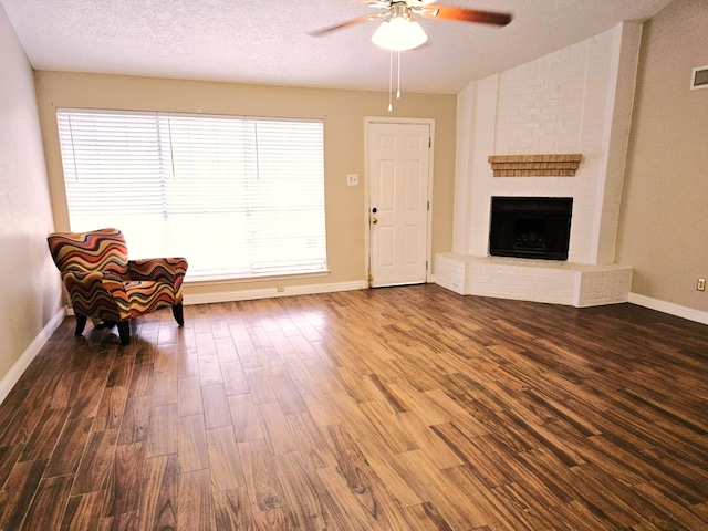 unfurnished room with a brick fireplace, dark wood-type flooring, a textured ceiling, and ceiling fan