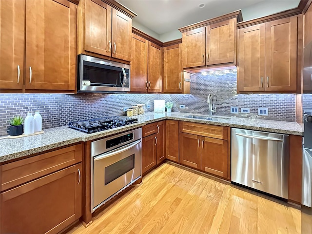 kitchen featuring sink, light stone counters, light wood-type flooring, stainless steel appliances, and decorative backsplash