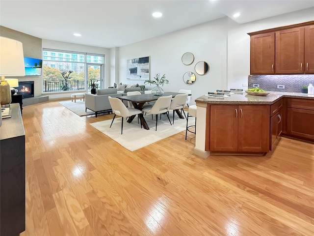 kitchen featuring decorative backsplash, a tile fireplace, kitchen peninsula, and light wood-type flooring