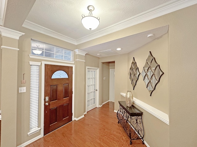 foyer entrance featuring ornamental molding, hardwood / wood-style floors, a textured ceiling, and ornate columns