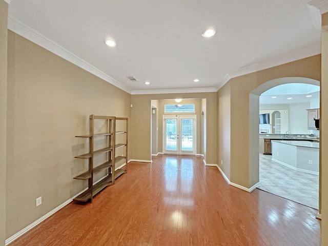 unfurnished room with crown molding, sink, light wood-type flooring, and french doors