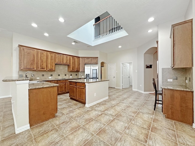 kitchen with a breakfast bar, sink, stainless steel fridge with ice dispenser, kitchen peninsula, and light stone countertops