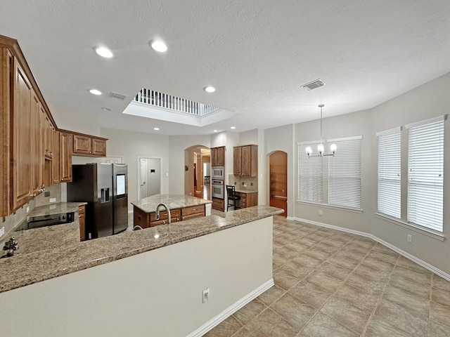 kitchen with appliances with stainless steel finishes, light stone counters, a kitchen island, decorative light fixtures, and a chandelier