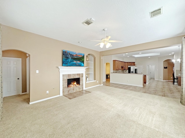 unfurnished living room featuring built in shelves, a fireplace, light colored carpet, and ceiling fan