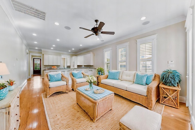 living room with crown molding, ceiling fan, and light wood-type flooring