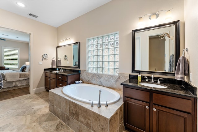 bathroom featuring tiled bath, a healthy amount of sunlight, and vanity