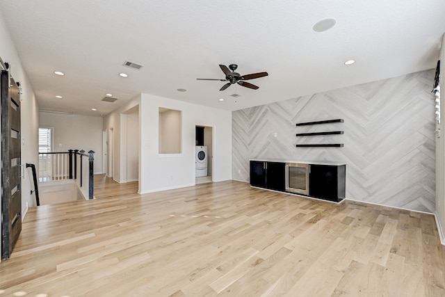 unfurnished living room featuring ceiling fan, light hardwood / wood-style flooring, a barn door, and washer / clothes dryer