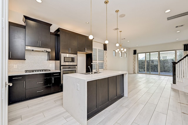 kitchen with decorative light fixtures, stainless steel appliances, an island with sink, sink, and backsplash