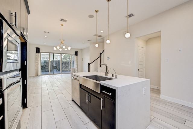 kitchen with an island with sink, stainless steel appliances, hanging light fixtures, light hardwood / wood-style flooring, and sink