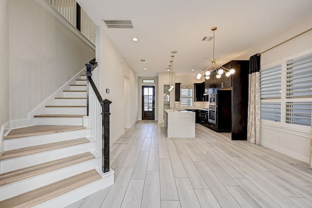 kitchen with decorative light fixtures, light hardwood / wood-style floors, stainless steel double oven, and a center island