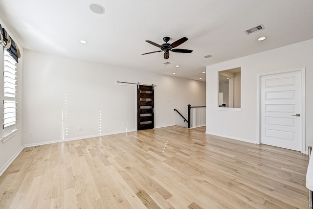 unfurnished room featuring ceiling fan, a barn door, light wood-type flooring, and a healthy amount of sunlight