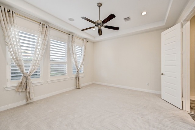 empty room with ceiling fan, light colored carpet, and a raised ceiling