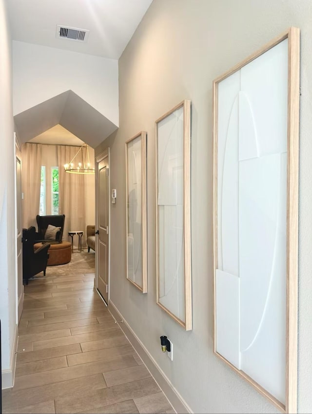 corridor with a chandelier, lofted ceiling, and hardwood / wood-style flooring