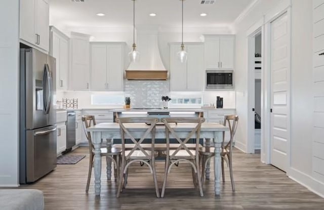 kitchen featuring hanging light fixtures, custom range hood, white cabinetry, hardwood / wood-style floors, and stainless steel appliances