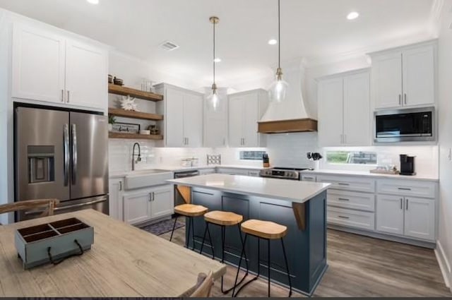 kitchen with stainless steel appliances, open shelves, a kitchen island, a sink, and backsplash