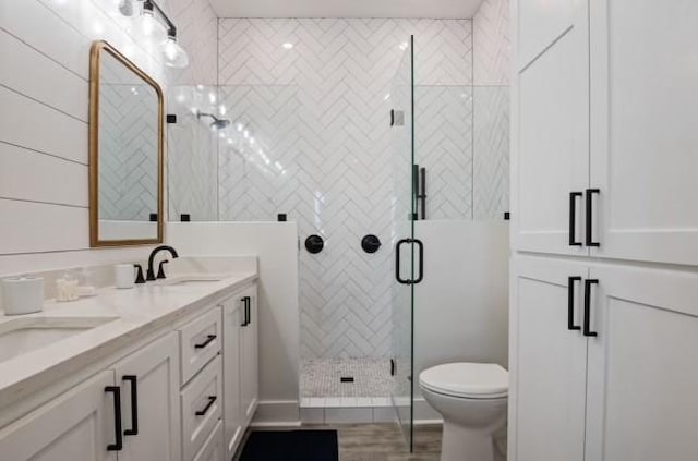 full bath featuring double vanity, a shower stall, toilet, and wood finished floors