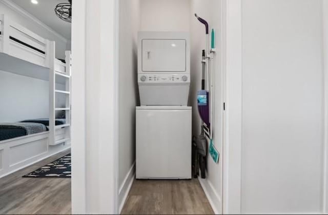 laundry area featuring wood-type flooring, stacked washer and clothes dryer, and crown molding