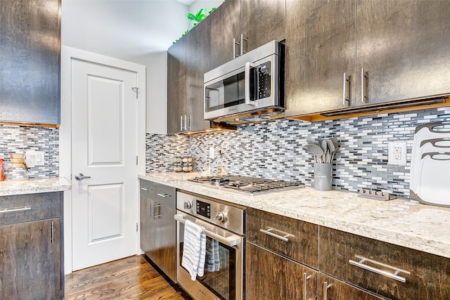 kitchen with tasteful backsplash, appliances with stainless steel finishes, light stone counters, and dark brown cabinetry